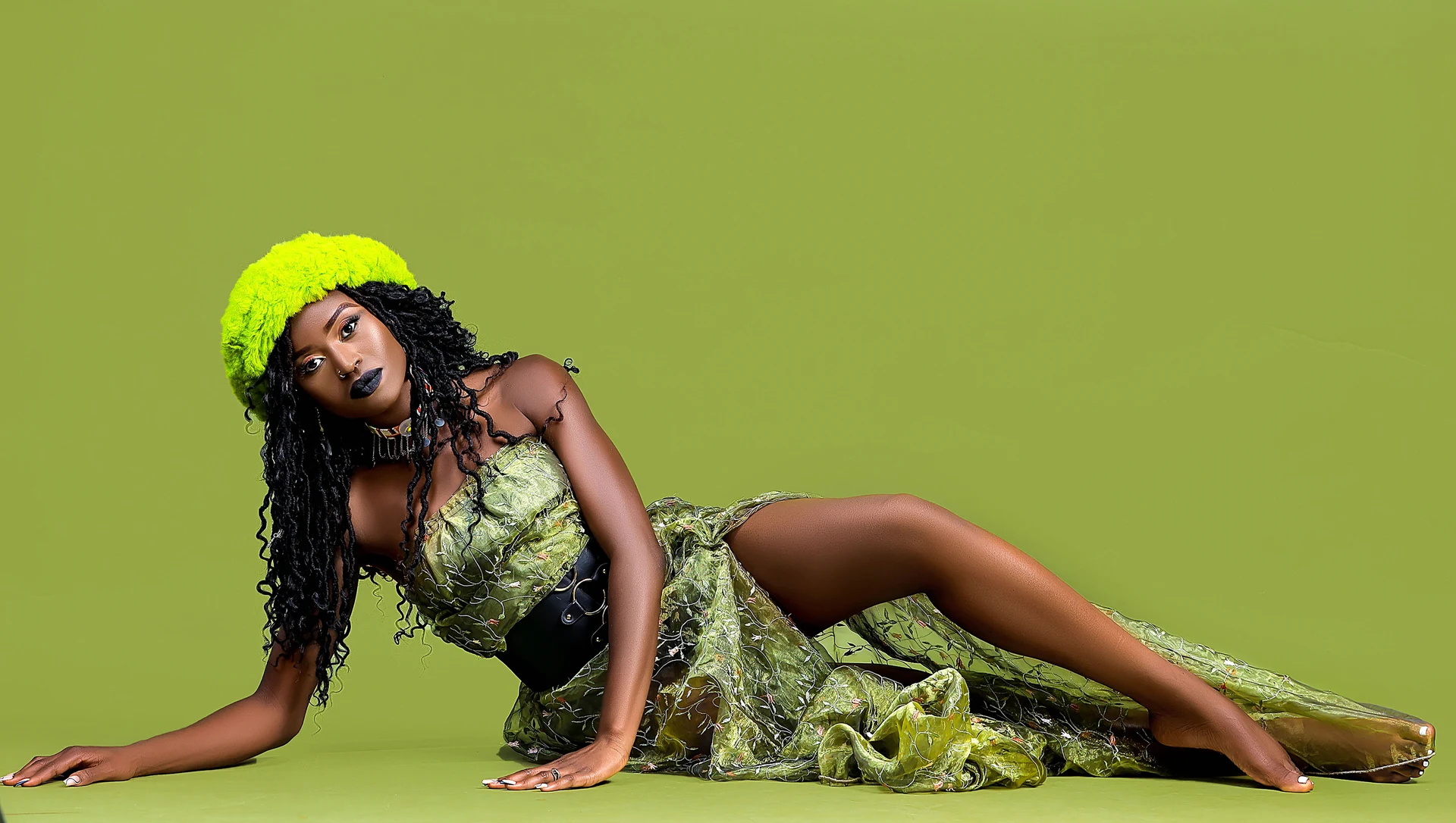Catu Diosis reclining in a green outfit against a green studio background.